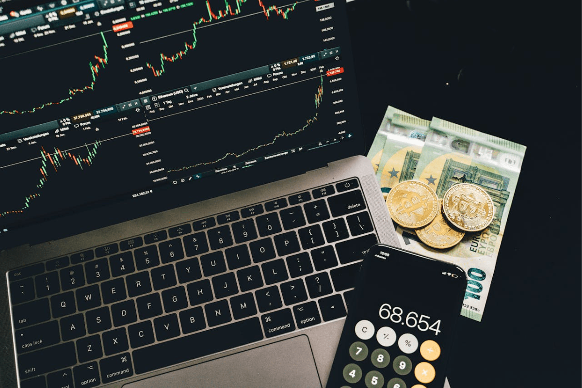 Laptop mit Bitcoin Kursdiagrammen, Euro-Scheinen und Bitcoin-Münzen